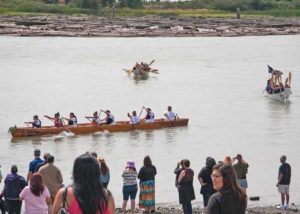 people standing on beach as canoers paddle by